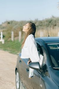 a woman leaning out of a car window, enjoying the fresh air with a relaxed expression on her face.