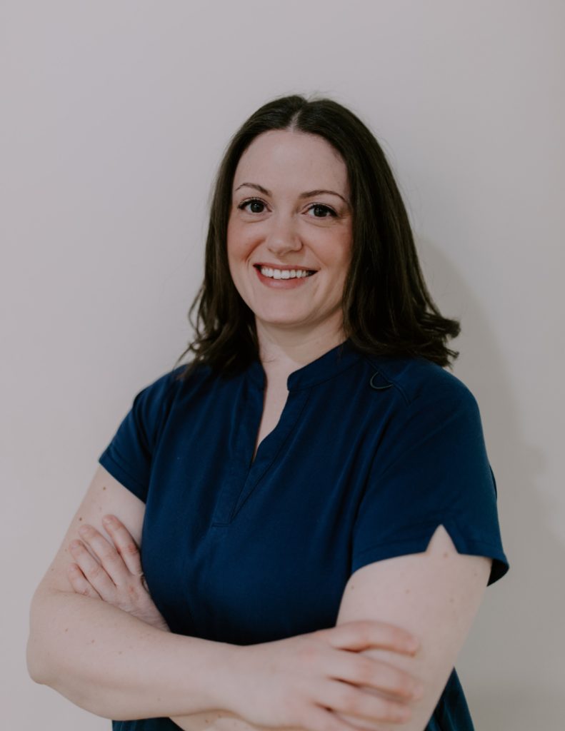 an acupuncturist standing with scrubs on and arms crossed smiling at the camera | massage and acupuncture near me 