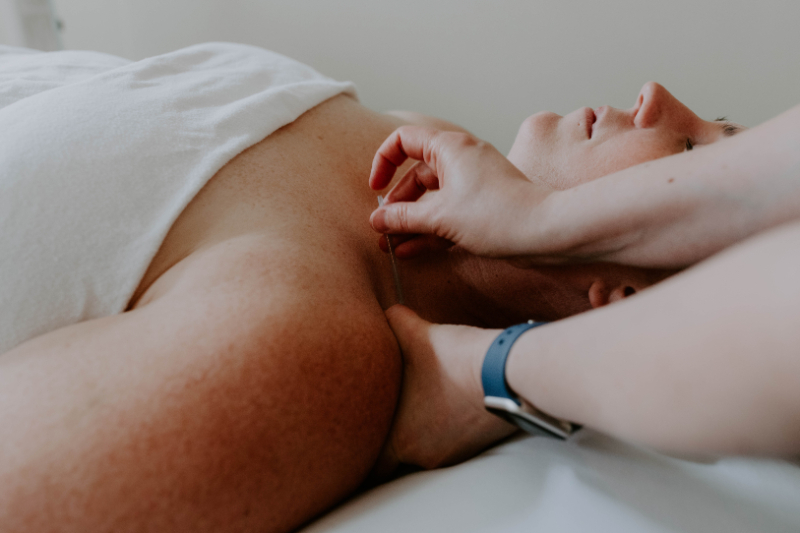 Person receiving upper body treatment with a needle during adenomyosis and acupuncture session in clinic.