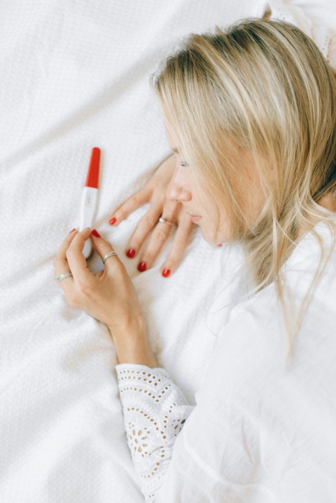 Woman lying on bed holding a pregnancy test, symbolizing fertility planning and hopeful conception journey.