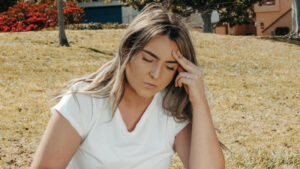 Woman sitting outdoors holding her jaw and forehead, possibly experiencing TMJ pain before acupuncture for TMJ pain.
