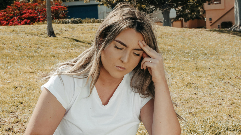 Woman sitting outdoors holding her jaw and forehead, possibly experiencing TMJ pain before acupuncture for TMJ pain.