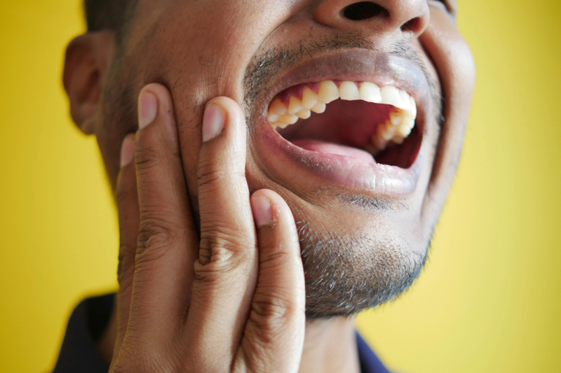 Man holding his jaw in pain with mouth open, showing possible need for acupuncture for TMJ pain relief.